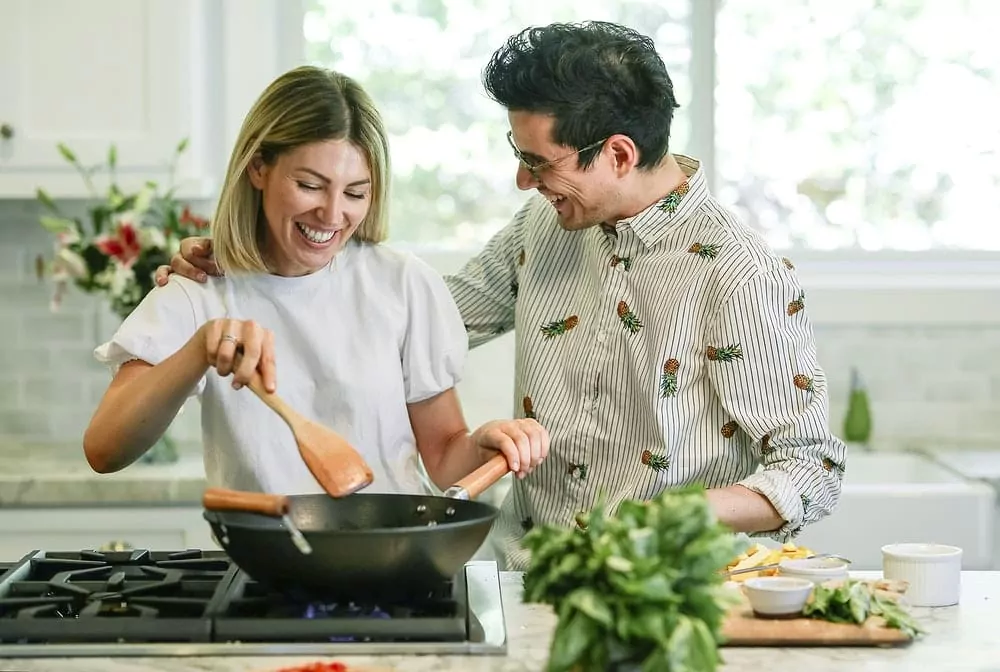 Une femme et un homme souriants préparant à manger à l'aide d'un wok