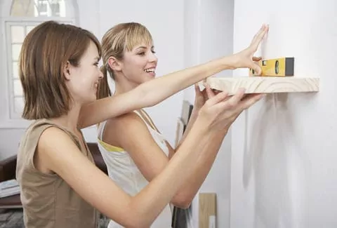 Deux femmes qui sont en train de fixer une étagère sur un mur